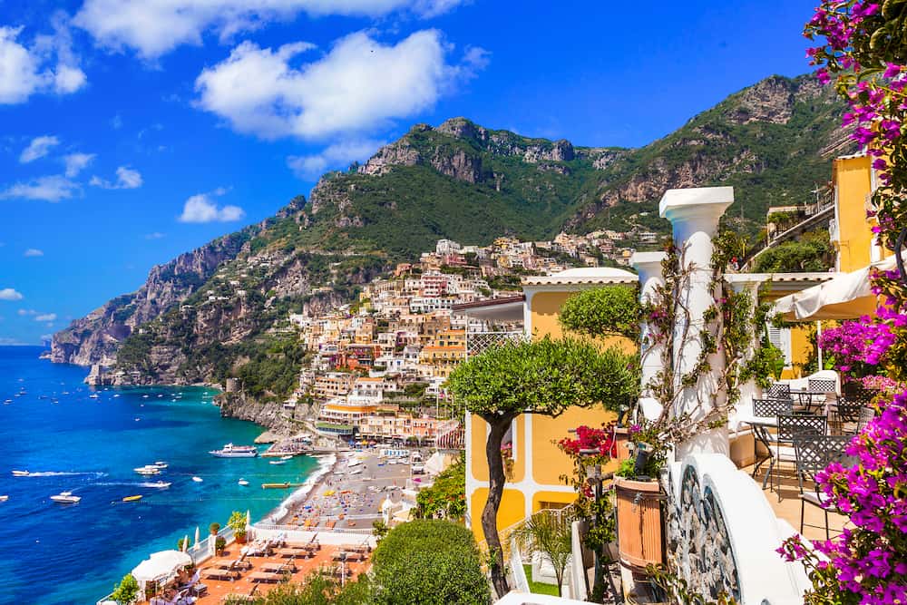 Beautiful view of the Amalfi Coast with bright yellow buildings, blooming purple flowers, and rugged green mountains