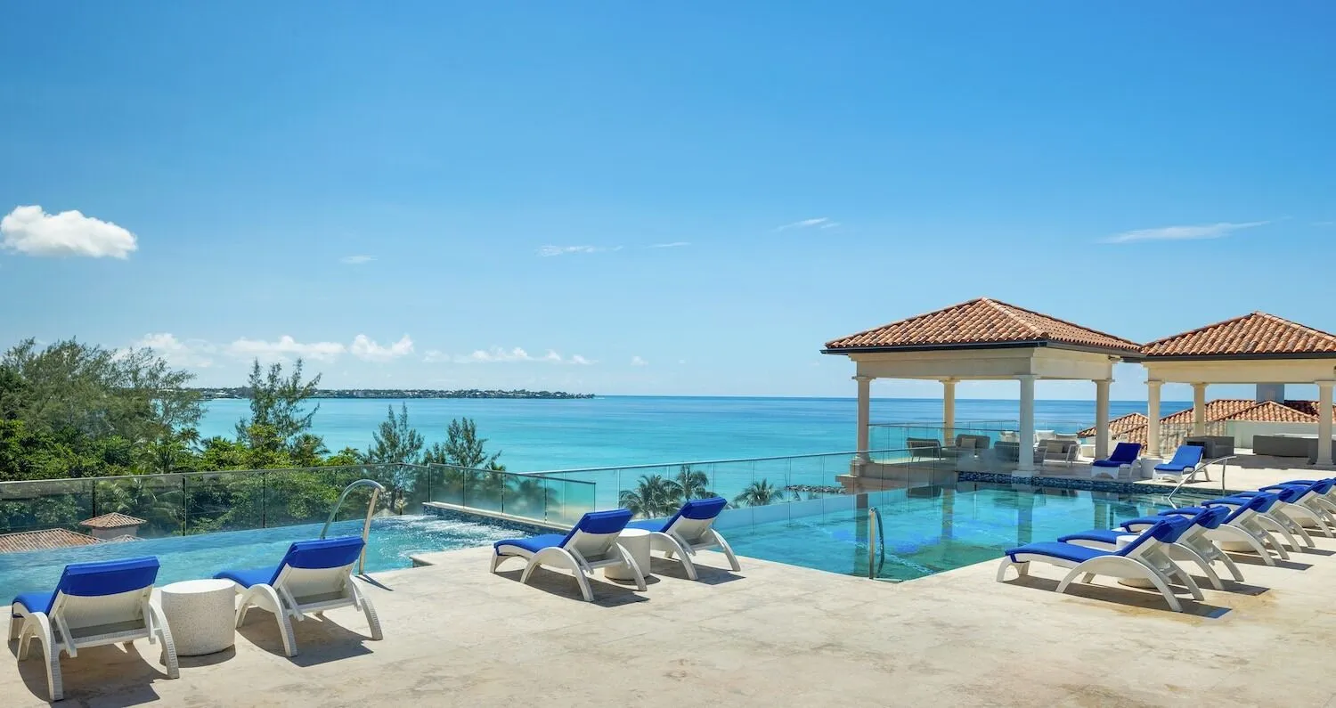 Tropical vacation setting with a rectangular pool, a white tiled deck, and blue water stretching to the horizon