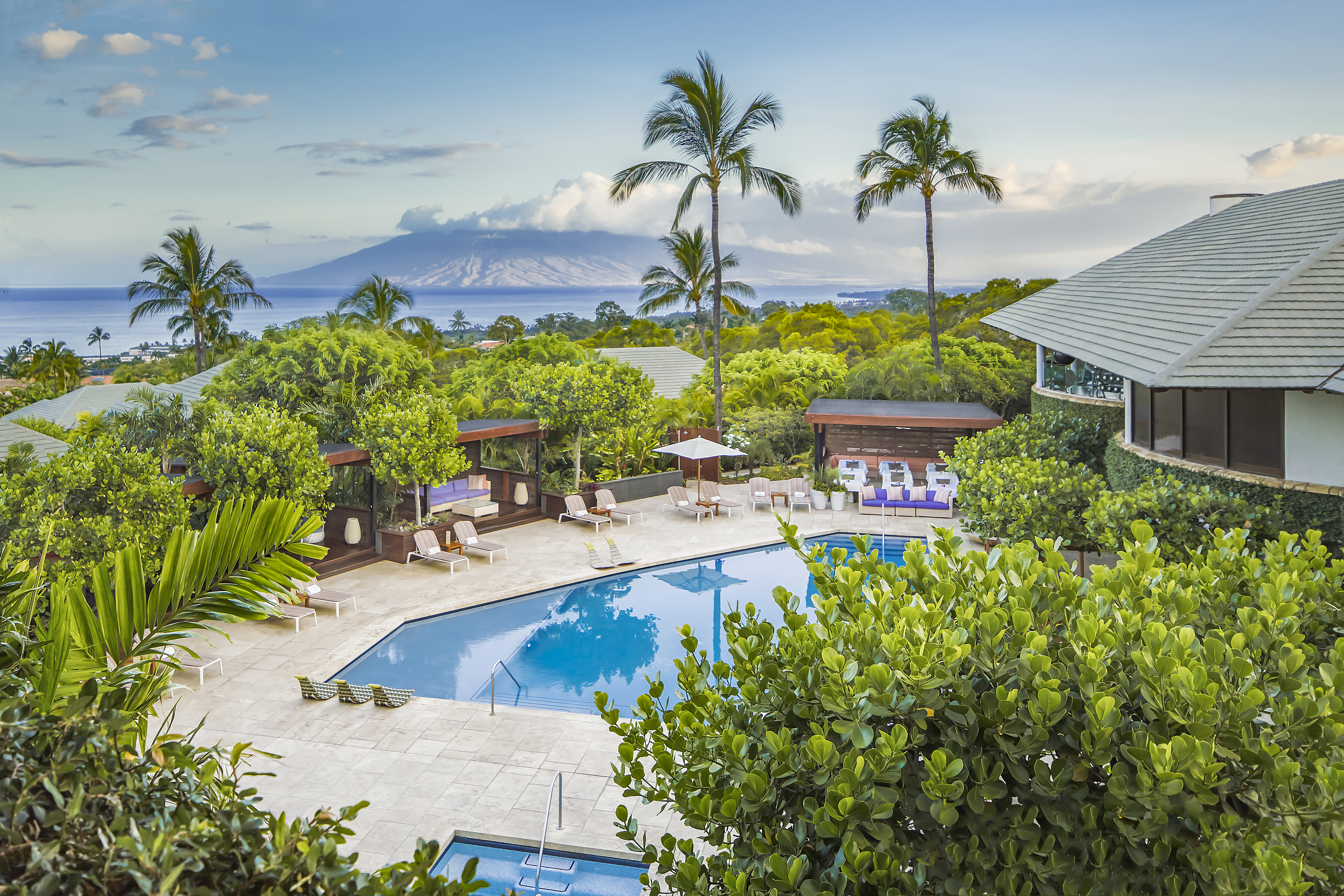 Estate grounds on a Hawaiian island with thick vegetation, a resort pool, and an island volcano visible on the horizon