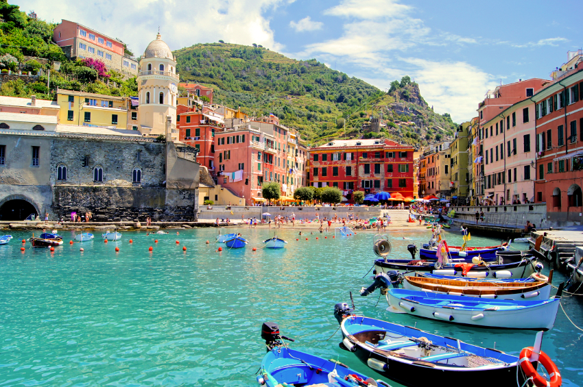 Bright sunny day view of Vernazza's waterfront, featuring the central square, a bell tower, and orange-roofed buildings