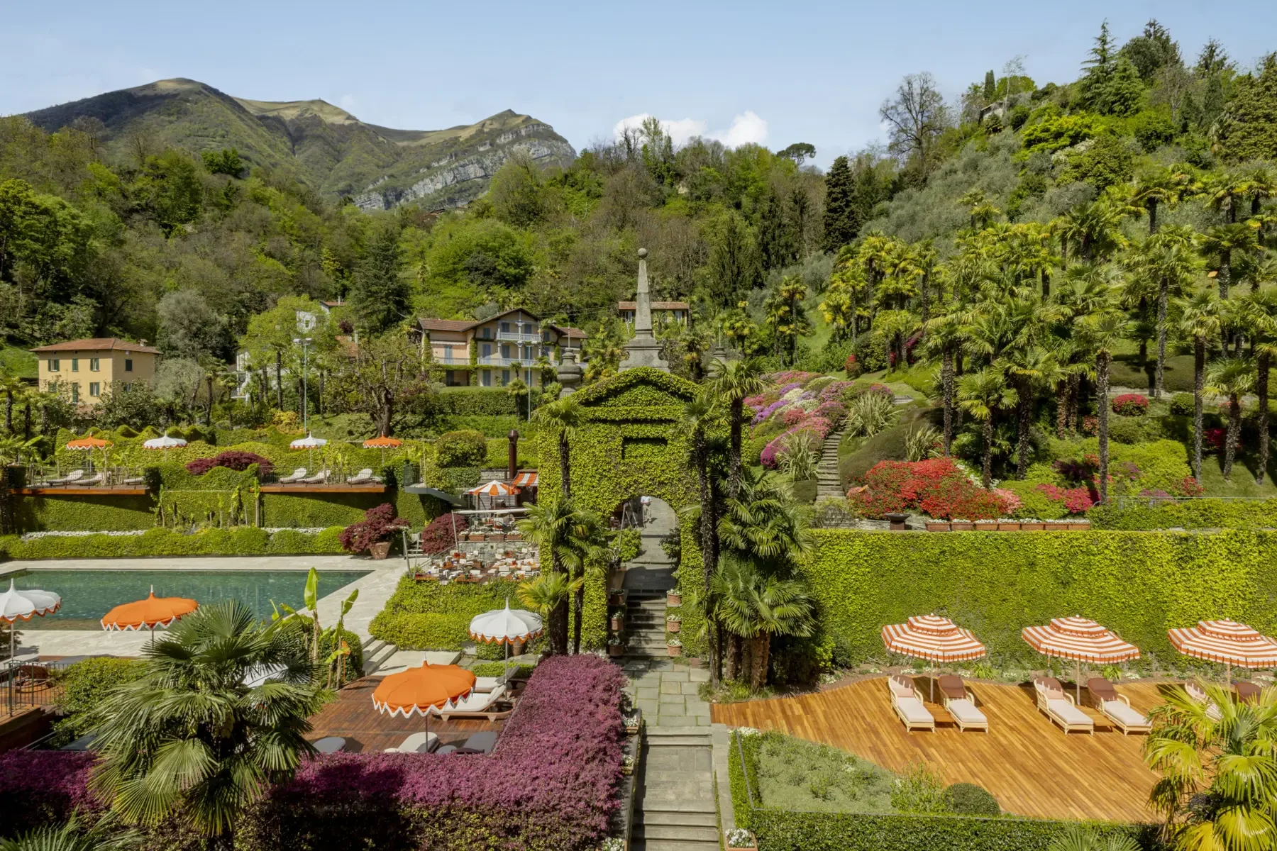 Luxurious lakeside resort with a swimming pool and sun loungers surrounded by vibrant, manicured Italian gardens